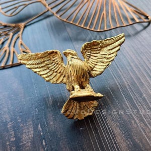 May include: A gold-colored eagle figurine with its wings spread wide. The eagle is perched on a base and has a detailed design.