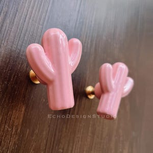 Op de afbeelding: Twee roze keramische cactus-ladegrepen met gouden metalen hardware. De cactus is een populair ontwerpelement voor thuisdecoratie.