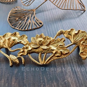Peut inclure: Une décoration en métal doré en forme de fleur de lotus avec des détails complexes. Le motif présente plusieurs feuilles de lotus et une fleur de lotus centrale.