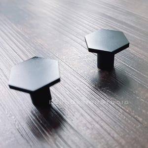 May include: Two black hexagonal cabinet knobs with a smooth, matt finish.