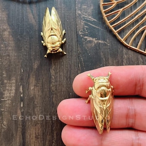 May include: Two gold cicada insect figurines. The cicadas are detailed and realistic, with textured wings and a shiny finish.