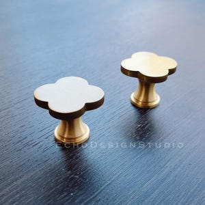 May include: Two gold-toned metal cabinet knobs shaped like a four-leaf clover. The knobs have a smooth, polished finish.