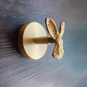 May include: A gold-toned wall hook featuring a rabbit head design. The hook is mounted on a round base.