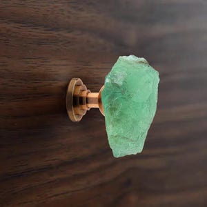 Puede incluir: Un pomo de armario de piedra preciosa verde con base de cobre. El pomo tiene forma de roca rugosa e irregular.