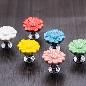 Puede incluir: Seis pomos de armario de cerámica con forma de flor en varios colores, incluyendo rojo, blanco, amarillo, azul, verde y rosa. Cada pomo tiene una base plateada.