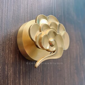 May include: Gold-toned metal cabinet knob with a stylised cloud design. The knob is mounted on a round base.