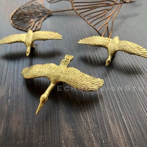 Peut inclure: Trois sculptures d'oiseaux en métal doré aux ailes déployées. Les oiseaux volent en formation sur un fond de bois foncé.