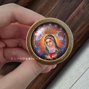 May include: A round, brass-colored, decorative knob with a glass insert featuring a colorful image of the Virgin Mary with a crown of stars and angels. The image is set against a dark blue background with gold accents.