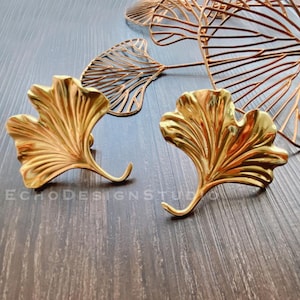 May include: A pair of gold-tone earrings shaped like ginkgo leaves. The earrings have a hook closure.