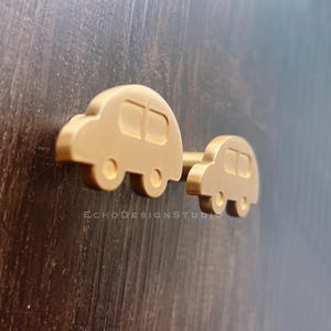 May include: Gold-colored cabinet pull in the shape of two connected cartoon cars. The larger car is in front of the smaller car. The text "ECHODESIGNSTUDIO" is at the bottom of the image.