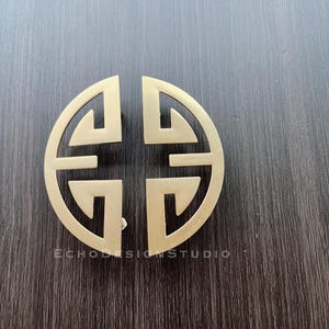May include: A gold-colored metal door knob with a circular design featuring a traditional Chinese symbol.