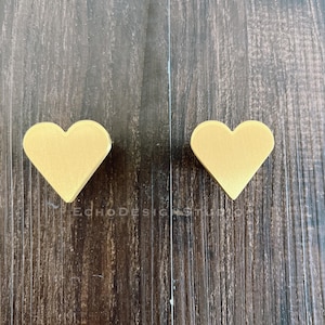 May include: Two gold heart-shaped cabinet knobs on a wood background.