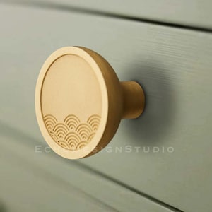 May include: A round wooden cabinet knob with a carved wave pattern in a light brown color.
