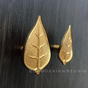May include: Two gold leaf-shaped cabinet knobs with a textured surface.