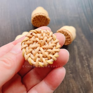 Pode incluir: Close-up de um puxador redondo de rattan tecido, castanho claro e com superfície texturizada. Duas outras puxadores semelhantes estão no fundo. O texto "ECHODESIGNSTUDIO" é visível. Provavelmente puxadores de móveis.