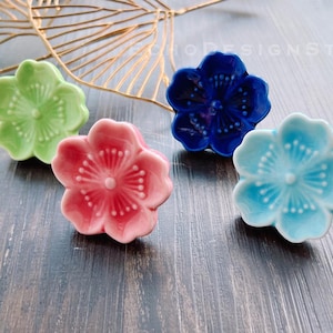 Puede incluir: Cuatro pomos de cerámica con forma de flor en verde, rosa, azul y azul claro. Los pomos tienen un diseño en relieve y son perfectos para añadir un toque de fantasía a los muebles.