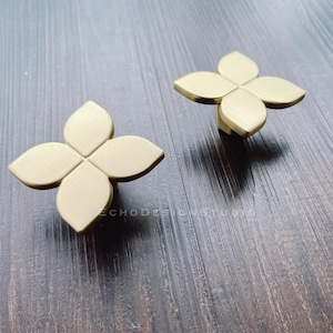 May include: Two gold-toned metal flower-shaped drawer pulls. Each pull has five points and a brushed finish.