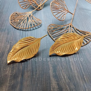 May include: A pair of gold leaf-shaped earrings. The earrings are made of metal and have a textured surface.