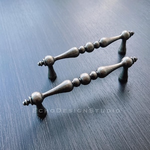 Może przedstawiać: Dwa srebrne gałki do szafek z koralikowym wzorem. Gałki mają zaokrąglony, lekko spiczasty koniec.