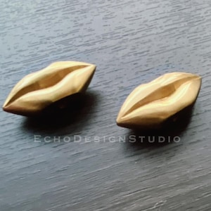May include: Two gold-colored lip-shaped earrings. The earrings are smooth and have a shiny finish.