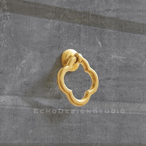 Könnte beinhalten: Ein goldfarbener Metall-Schubladengriff mit einem Kleeblatt-Design.