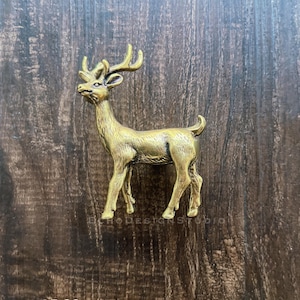 Könnte beinhalten: Eine detaillierte, messingfarbene Hirschfigur mit Geweih. Der Hirsch steht, der Kopf leicht nach links gedreht. Die Figur hat eine strukturierte Oberfläche und ist wahrscheinlich aus Metall gefertigt. Das Design ist realistisch und detailliert.