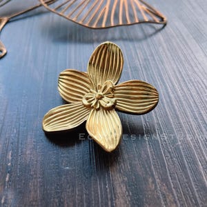 以下が含まれることがあります： 金色の金属製のフラワー型の小物入れ。皿は、隆起した線と中央の小さな花で詳細なデザインになっています。