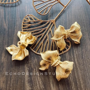 Peut inclure: Trois poignées de tiroir en métal doré en forme de nœuds. Les poignées ont une surface texturée et sont disposées sur une surface en bois.