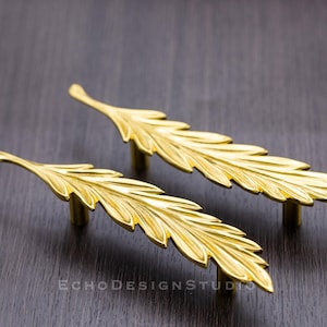 May include: Two gold leaf-shaped cabinet pulls with a detailed design.