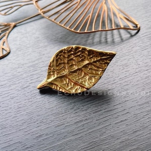 May include: A gold leaf-shaped decorative object with a detailed textured surface. The leaf is made of metal and has a realistic appearance.