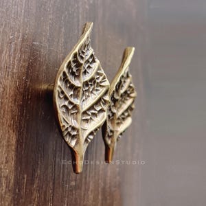 May include: Two gold leaf-shaped cabinet knobs with a detailed, textured design.