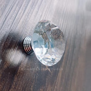 May include: A clear crystal cabinet knob with a silver base. The knob has a faceted design and is a decorative accent for furniture.