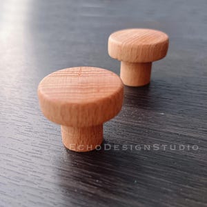 May include: Two wooden knobs with a natural finish. The knobs are round and have a slightly raised edge. They are about 1 inch in diameter.