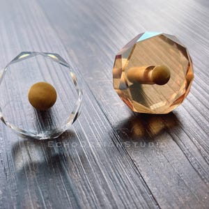 Puede incluir: Dos sellos de vidrio transparente con un diseño redondeado y facetado. Un sello tiene un mango de madera marrón y el otro tiene una bola marrón en su interior.