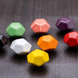 Może przedstawiać: Osiem kolorowych, geometrycznych ceramicznych gałek do szuflad w różnych kolorach, w tym czarny, zielony, biały, pomarańczowy, żółty, czerwony, fioletowy i różowy.