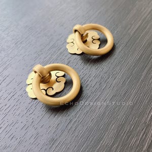 May include: Two gold-toned metal drawer pulls with a ring handle and a decorative cloud design.