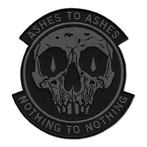Puede incluir: Un parche negro con un diseño de calavera y las frases "ASHES TO ASHES" y "NOTHING TO NOTHING" dispuestas en círculo. La calavera tiene cuencas de ojos en forma de lágrima.