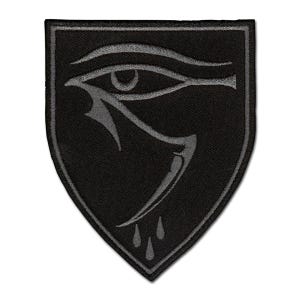 May include: A shield-shaped embroidered patch featuring a black background with a dark gray stylized Eye of Horus design. The emblem includes a prominent eye symbol with a downward-pointing tail and three small teardrop shapes below the eye.