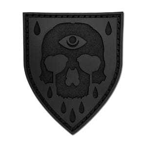 May include: A black shield-shaped patch featuring an embossed design of a skull with a third eye on its forehead. The skull is surrounded by multiple teardrop shapes, with two drops falling from the eye sockets. The border has a stitched edge.