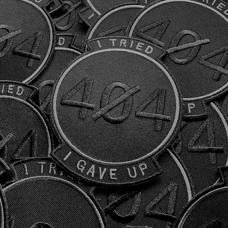 K&ouml;nnte beinhalten: Eine Ansammlung schwarzer, gestickter Aufn&auml;her. Jeder runde Aufn&auml;her zeigt die durchgestrichene Zahl 404 und die wei&szlig;en Schriftz&uuml;ge &bdquo;I Tried&ldquo; und &bdquo;I Gave Up&ldquo;. Die Aufn&auml;her sind mit einem wei&szlig;en Rand versehen.