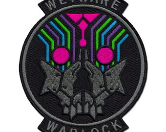 Op de afbeelding: Een ronde geborduurde patch met een zwarte achtergrond met de tekst WETWARE bovenaan en WARLOCK onderaan. Het midden toont een gestileerd grijs schedelontwerp met felroze ronde ogen en neonblauwe, groene en paarse lijnen.