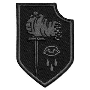 May include: Black and grey embroidered patch in a shield shape. The patch features a fist holding a sword, an eye with teardrops, and a grey border.