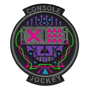 Peut inclure: Un écusson brodé circulaire représentant un crâne violet avec une visière grise affichant un X et des points roses. L'écusson comprend des lignes de circuit vert néon et rose, des accents bleus et le texte CONSOLE JOCKEY en lettres grises.