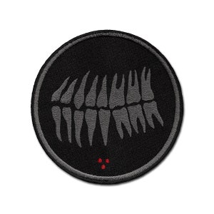 May include: A black and grey embroidered patch featuring a row of teeth and three red dots in the centre.