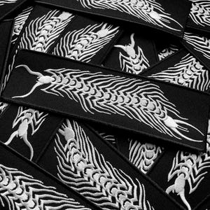 May include: A collection of black rectangular patches featuring a white embroidered dragon motif. The dragon has a detailed, flowing design. The patches are arranged in a layered pattern. These patches could be used to decorate clothing or accessories.