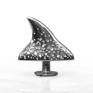 May include: A silver shark fin shaped bottle opener with a textured surface. The opener has a screw-on base.