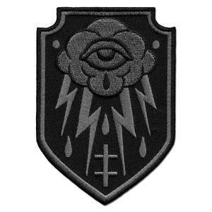 May include: Black and gray embroidered patch with a shield shape. The patch features a stylized cloud with an eye in the center, surrounded by lightning bolts and raindrops. A cross is at the bottom of the patch.