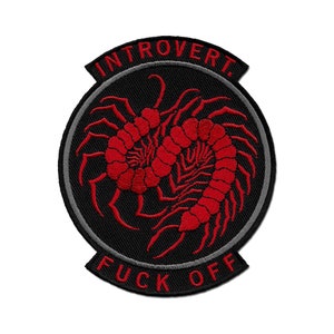 May include: Embroidered patch with a black background, a gray border, and red centipede-like creatures. The patch has the text "INTROVERT" at the top and "FUCK OFF" at the bottom in red. The patch is circular in shape.