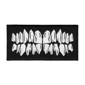 Könnte beinhalten: Ein rechteckiger schwarzer Aufnäher mit einem weißen, gestickten Design eines Gebisses. Die Zähne sind detailliert, mit einzelnen Zahnformen, was ein realistisches und leicht beunruhigendes Aussehen erzeugt. Der Aufnäher ist wahrscheinlich für Kleidung oder Accessoires.