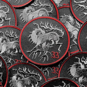 May include: Close-up of several black embroidered patches with a silver-grey design of a mythical creature with antlers and the number 33. The patches have a red border.